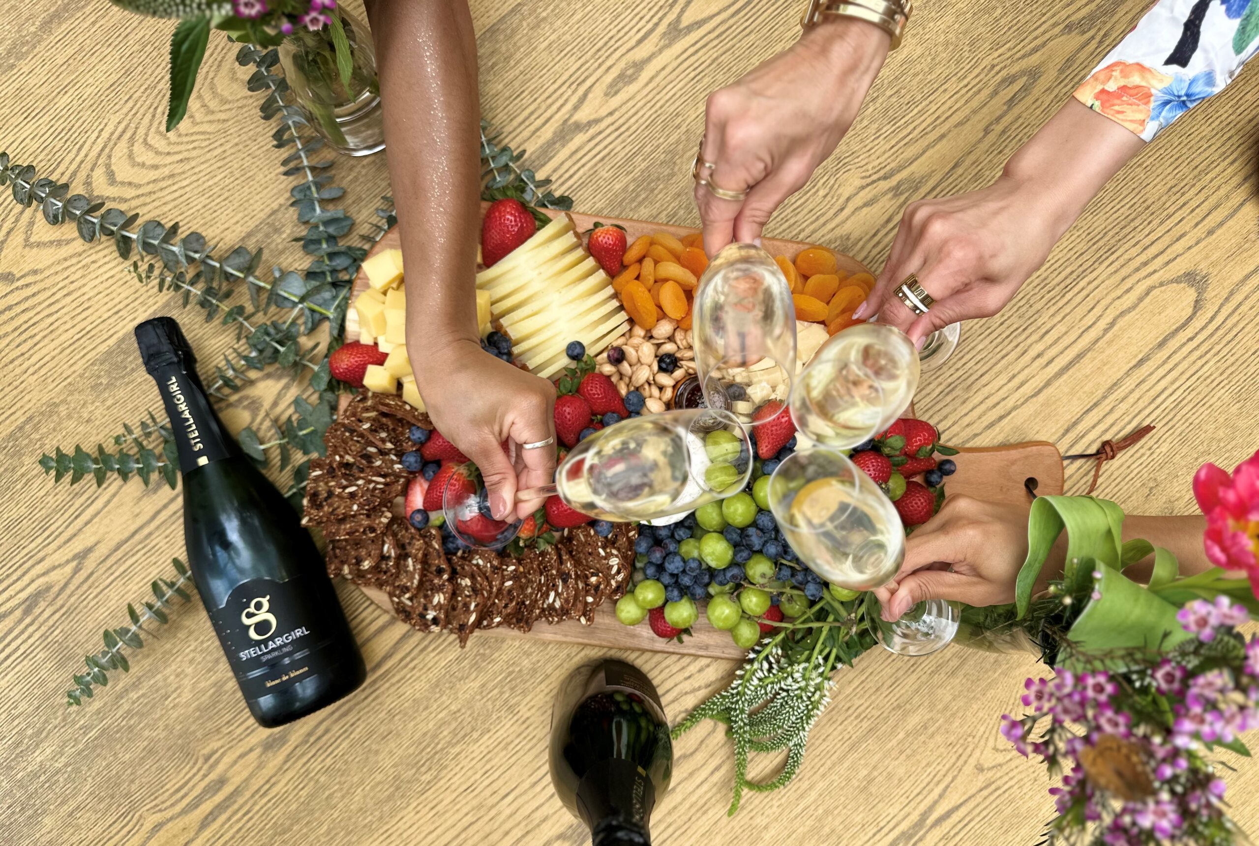 Group of ladies raising a glass of stellargirl champagne over a grazing board of snacks